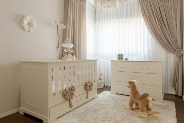 Nursery bayi bernuansa krem dengan tempat tidur, laci, dan kuda mainan
